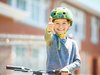 Ein Kind mit Helm und Velo strahlt mit hochgerecktem Daumen in die Kamera
