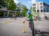 Schüler absolviert auf dem Schulhausplatz einen Parcours mit seinem Velo. Er ist sehr konzentriert, um den Ball richtig zu platzieren.