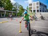 Schüler absolviert auf dem Schulhausplatz einen Parcours mit seinem Velo. Er ist sehr konzentriert, um den Ball richtig zu platzieren.