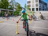 Schüler absolviert auf dem Schulhausplatz einen Parcours mit seinem Velo. Er ist sehr konzentriert, um den Ball richtig zu platzieren.